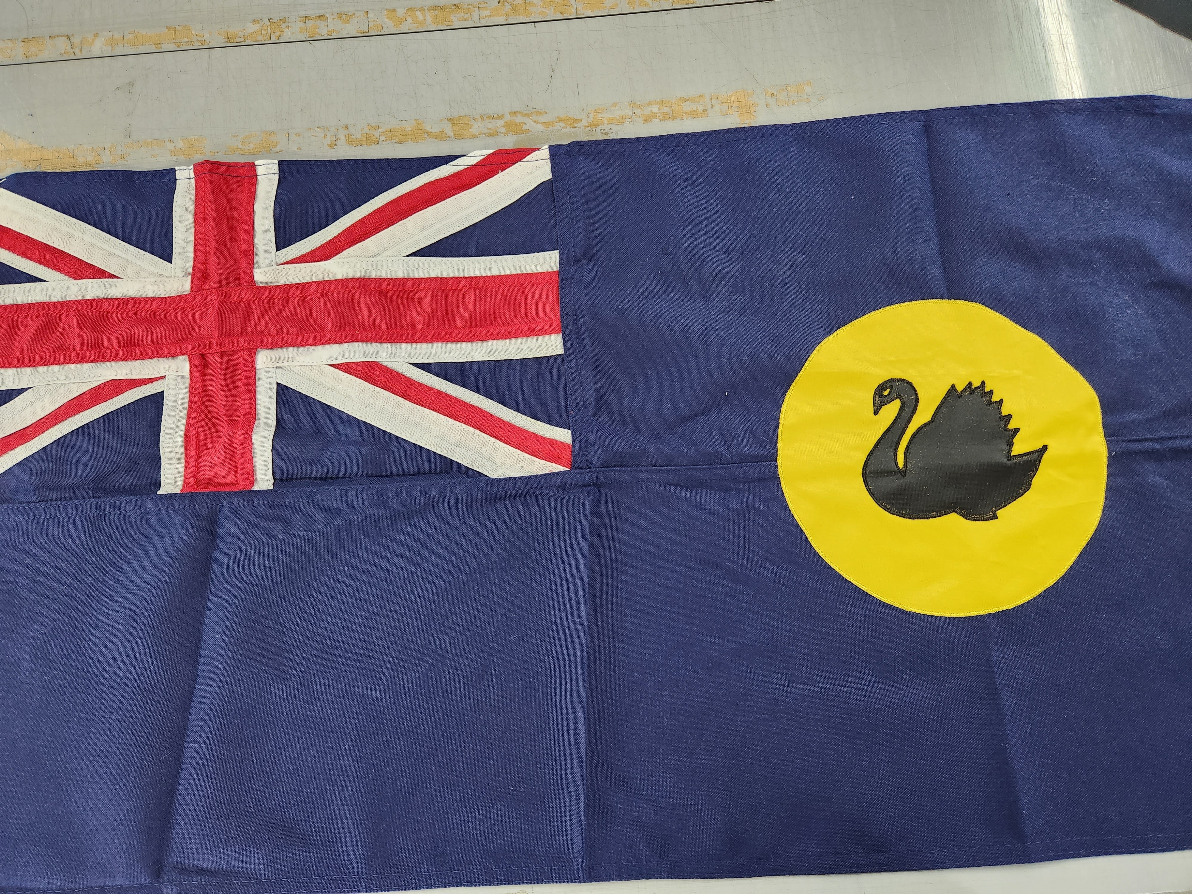 Flag with Union Jack and yellow circle with black swan emblem on blue background